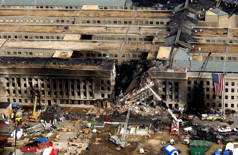 Pentagon building damaged after the 9/11 attacks, showing smoke rising from the impact site with emergency response teams on scene – a powerful reminder of one of the darkest days in American history.